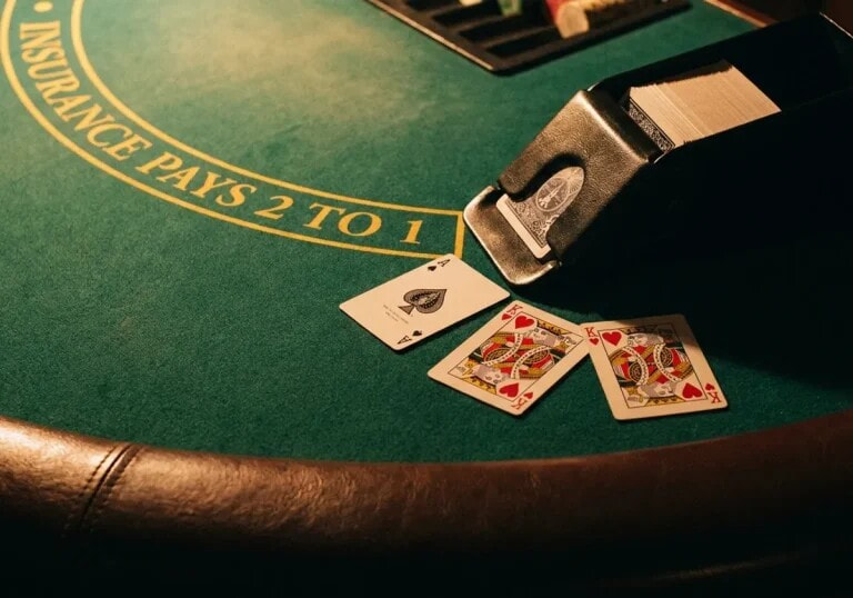 A blackjack table: an ace and two face cards face up on green baize beside the dealer's card shoe