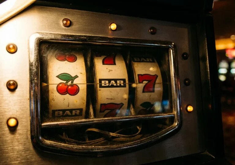 The three reels of a physical slot machine behind glass, showing cherries, a bar and a seven